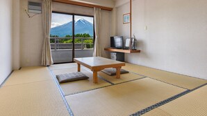 A room with tatami flooring, a low wooden table, a television on a shelf, and a view of a mountain through a sliding door. - SEMINAR PLAZA ROYAL FUJI (Fujikawaguchiko)