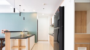 A modern kitchen with a black refrigerator, wooden cabinets, and a black countertop. - Fusion RiverGate Apart Infinity Pool (Ho Chi Minh City)