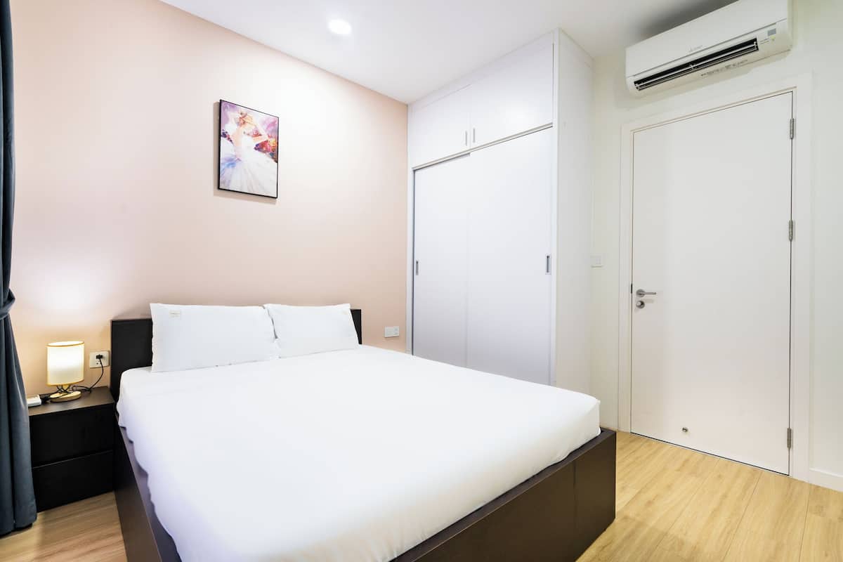 A hotel room with a bed, a nightstand with a lamp, a wardrobe, and an air conditioning unit.