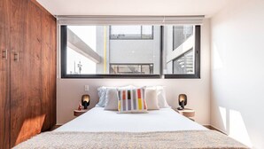 Ein Schlafzimmer mit großem Fenster, einem Bett mit weißer Bettwäsche, zwei Nachttischen mit Lampen und einem Holzschrank.