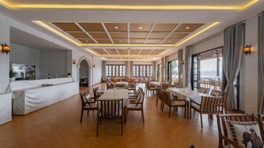 A spacious restaurant with wooden flooring, white tables, and chairs. It features a long counter with a bar area and large windows offering a view. - Relaxful Hotel (Luang Prabang)