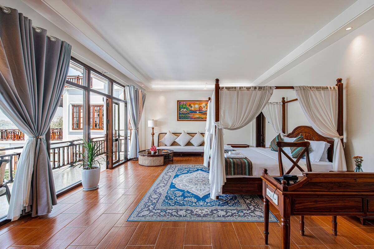 A spacious bedroom with a large bed, a wooden desk, and a balcony with curtains.