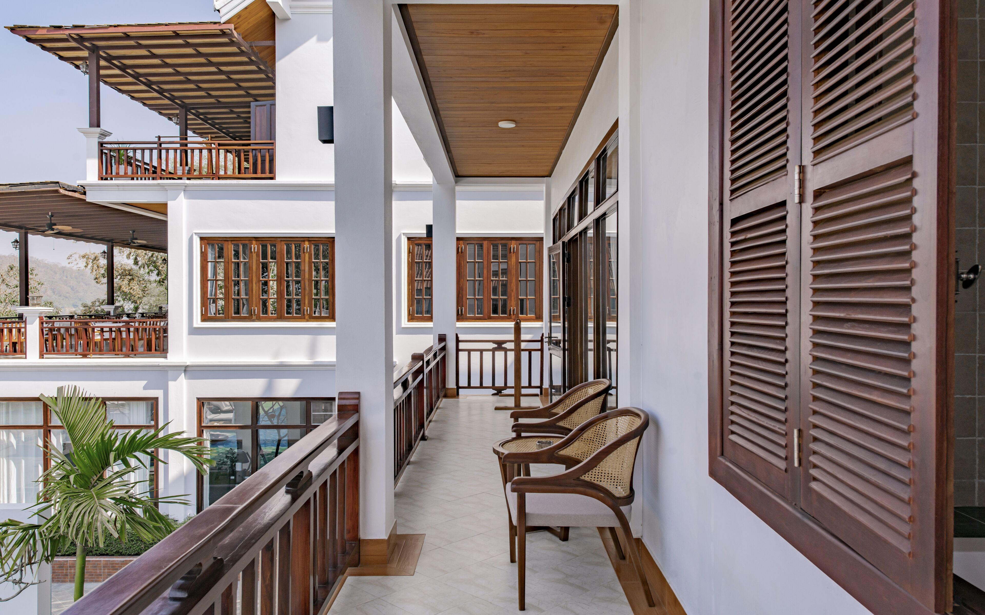 A balcony with wooden railings, wicker chairs, and large windows with shutters.