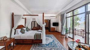 A spacious bedroom with a four-poster bed, a large window with a view, a sitting area with a table and chairs, and a bathroom with a sink and mirror. - Relaxful Hotel (Luang Prabang)