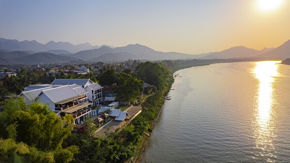 A riverside hotel with multiple buildings, a dock, and mountains in the background. - Relaxful Hotel (Luang Prabang)