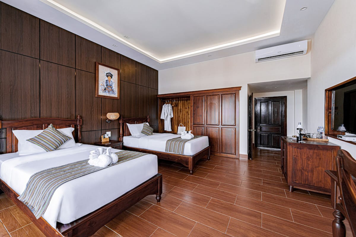 A hotel room with two beds, wooden paneling, a framed picture, a robe rack, and a TV.