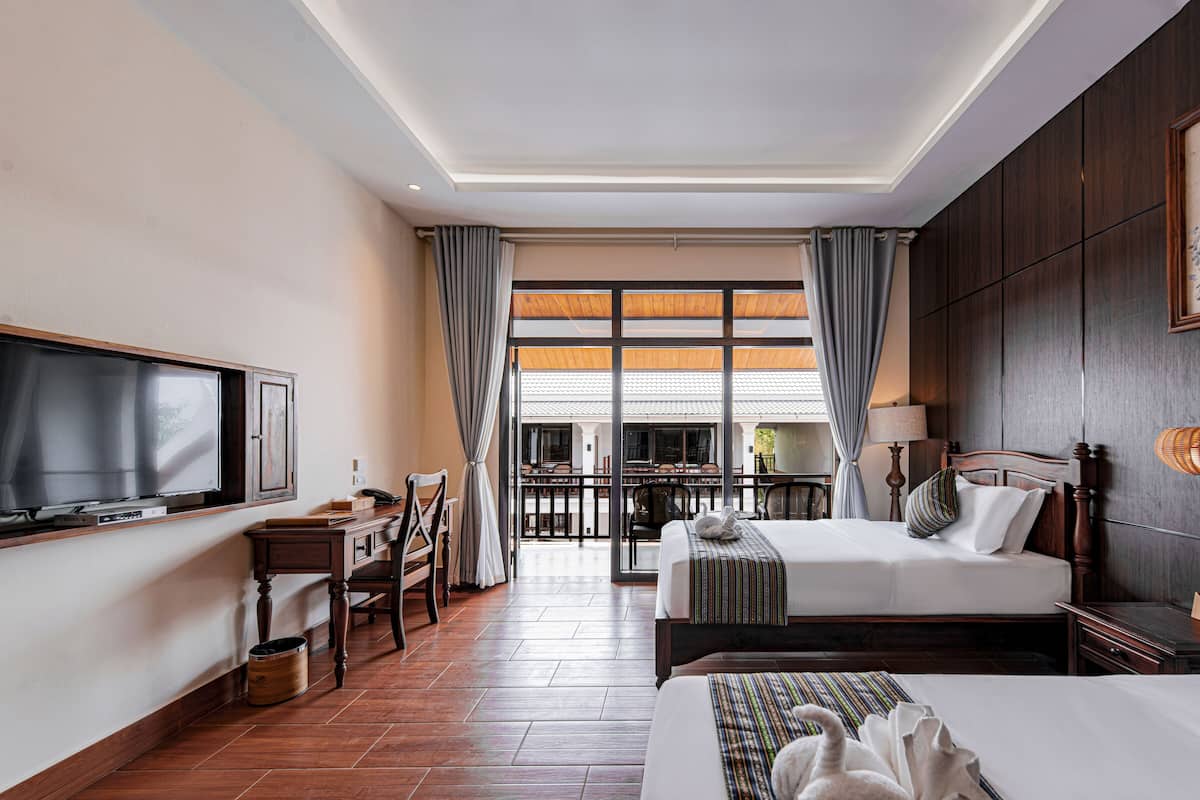 A hotel room with a large TV, a desk, a bed, and a view of the outdoor area.