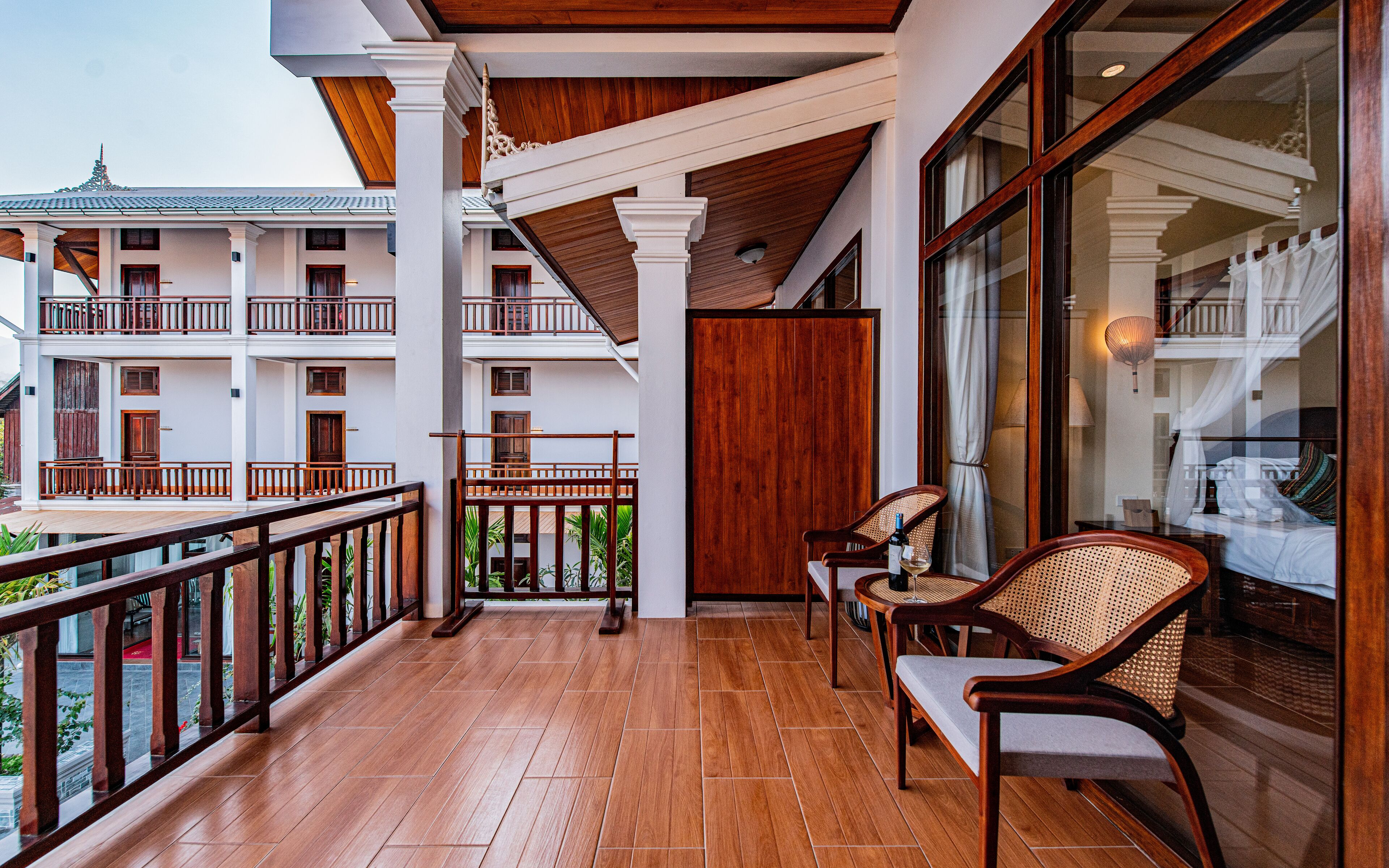 A balcony with wooden flooring, white railings, and a view of a multi-story building with balconies and windows.