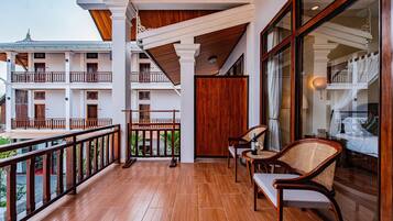 A balcony with wooden flooring, white railings, and a view of a multi-story building with balconies and windows.