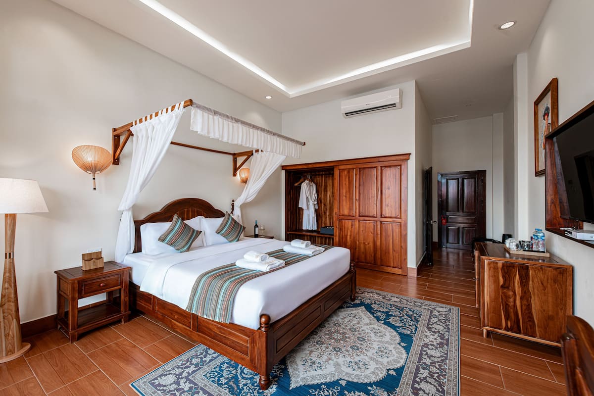A spacious bedroom with a four-poster bed, wooden wardrobe, and a large mirror.