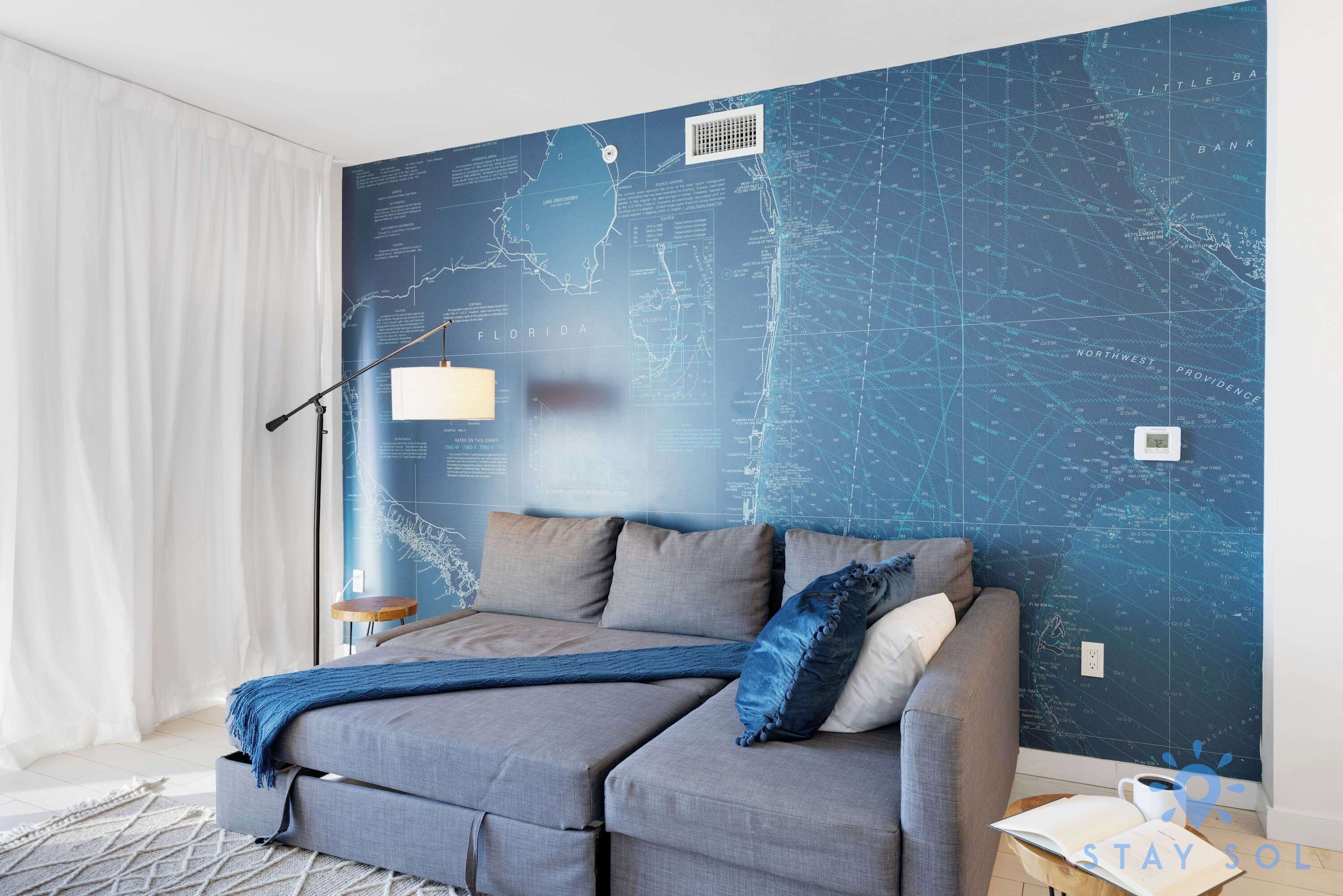 A modern bedroom with a large bed, a map wall, and a small table with a book and a cup.