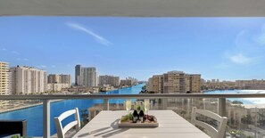 Un balcon avec une table dressée pour deux personnes, offrant une vue sur un port de plaisance et le paysage urbain.