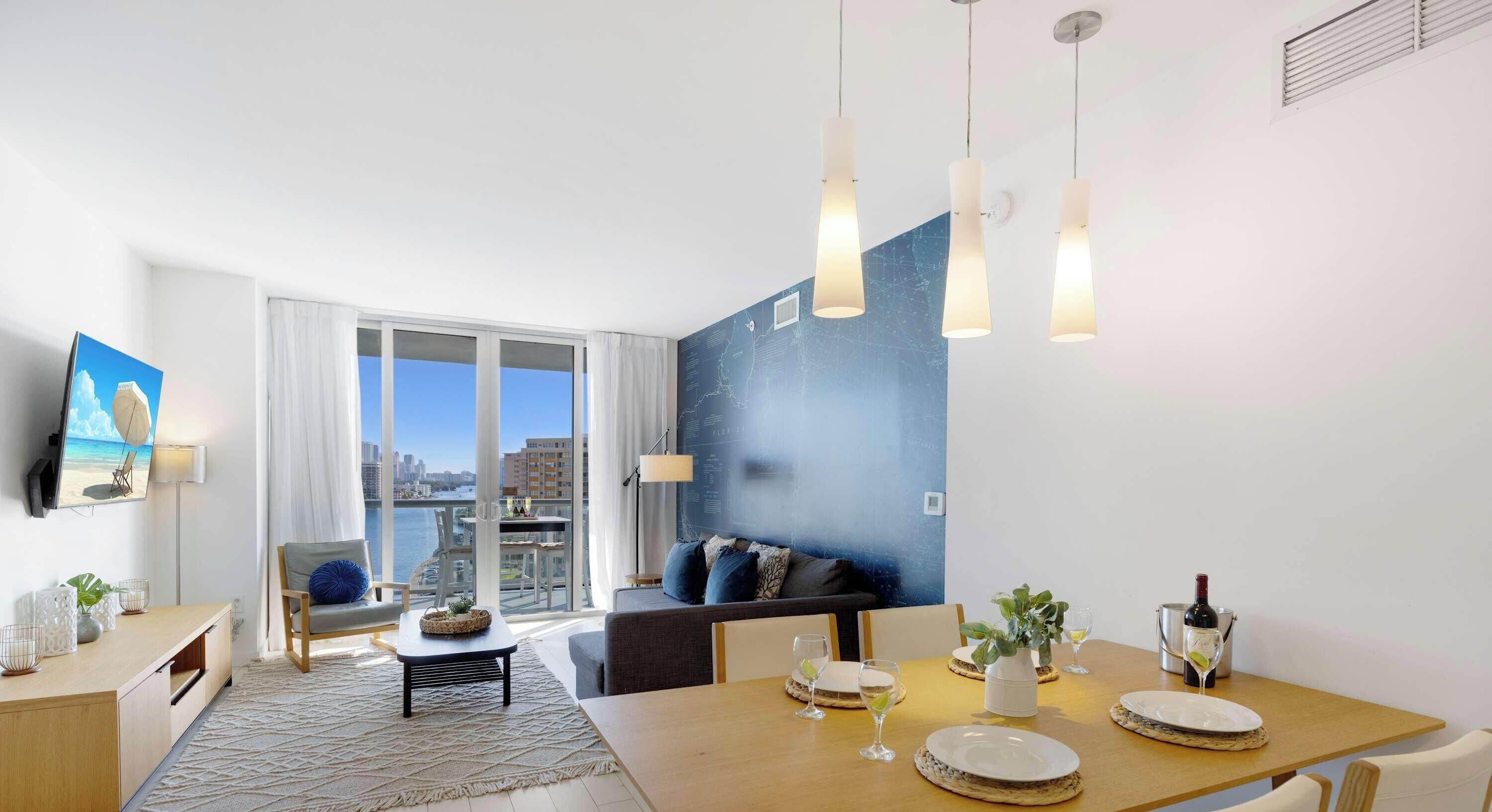 A modern living room with a large window, a dining area with a table set for two, and a cozy seating area with a sofa.