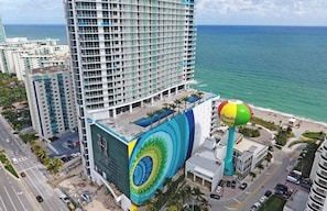 A high-rise hotel with a large mural on the side, a beach ball sculpture, and a view of the ocean. - Beach view Luxury: Amazing Pool, Resort Amenities (Hollywood)