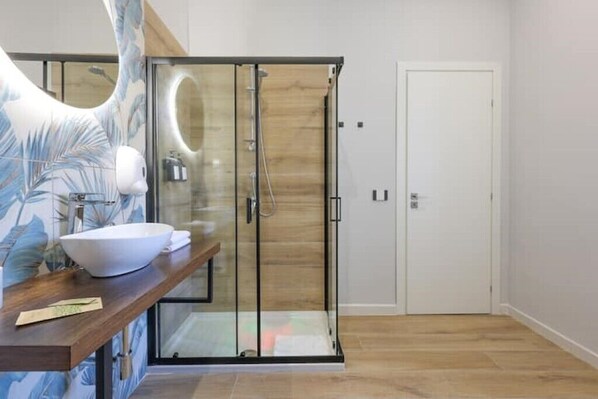 A modern bathroom with a glass-enclosed shower, a white sink, and a wooden vanity.