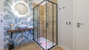 A modern bathroom with a glass-enclosed shower, a round mirror, and a wooden vanity with a white sink.