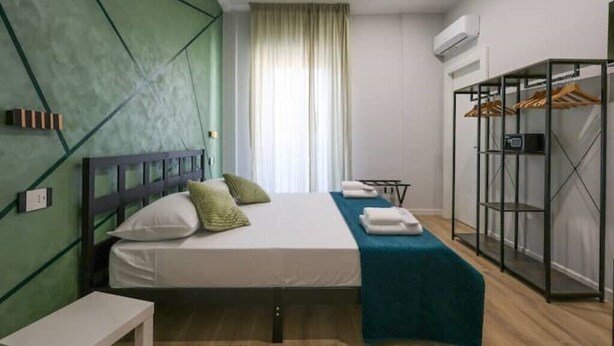 A modern hotel room with a bed, a bedside table, a wardrobe, and a window with curtains.
