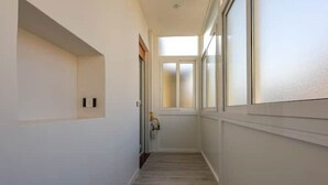 A narrow hallway with white walls and a wooden floor, leading to a door with frosted glass panels.