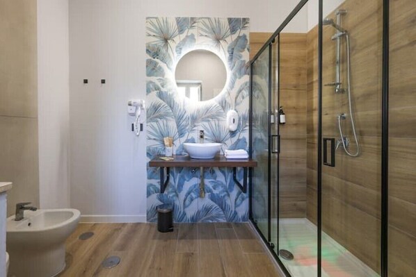 Une salle de bain moderne avec un plancher en bois, un lavabo sur pied, une douche à parois de verre et un mur décoratif agrémenté d’un miroir rond.