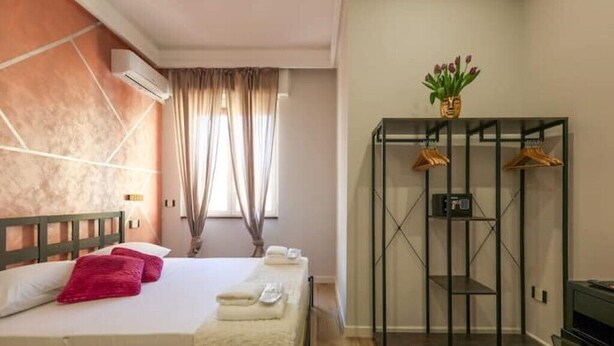 A hotel room with a bed, a wardrobe, a mirror, and a window with curtains.