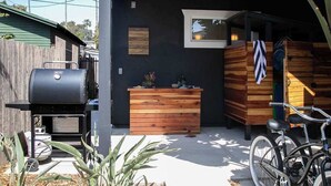 A modern outdoor kitchen area with a grill, wooden storage, and a bicycle. - Industrial-Inspired 2-Story California Beach House (Oceanside)