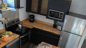 A modern kitchen with a wooden table set for a meal, a microwave, a refrigerator, and a stove. - Industrial-Inspired 2-Story California Beach House (Oceanside)