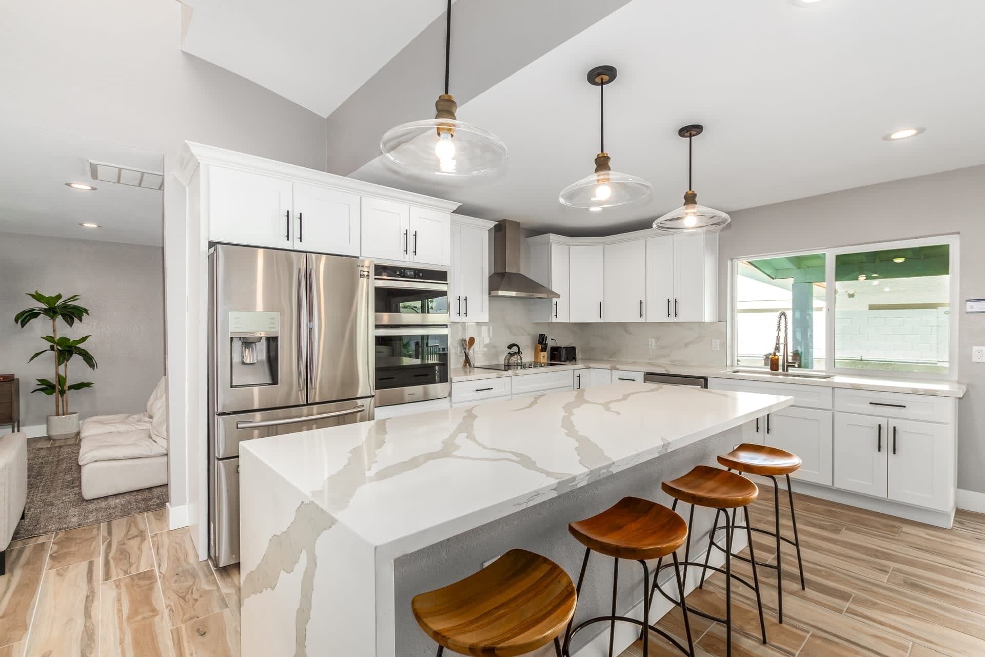 A modern kitchen with white cabinetry, stainless steel appliances, a marble island, and wooden bar stools.