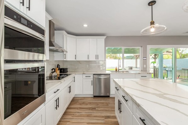 A modern kitchen with white cabinetry, stainless steel appliances, and a wooden floor.