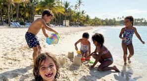 A beach with palm trees, a sandy shore, and people playing.