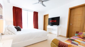 Ein Hotelzimmer mit einem Bett, einem Fernseher auf einem Schrank, einer Holztür und einem Fenster mit roten Vorhängen.