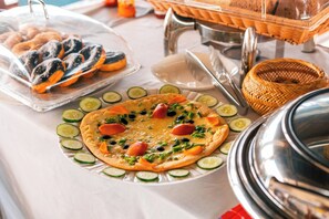 Una mesa de buffet con diversos alimentos, incluyendo pizza de verduras, pepinos en rodajas y una bandeja de pasteles.