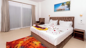 Une chambre d’hôtel avec un grand lit, une chaise, une petite table et un tableau représentant une scène de plage.