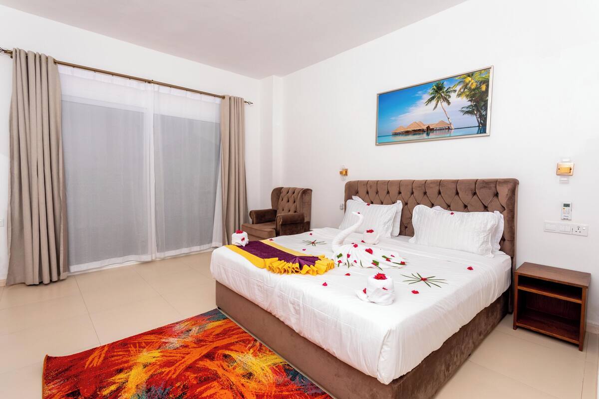 Ein Hotelzimmer mit einem großen Bett, einem Sessel, einem kleinen Tisch und einem Bild mit einer Strandansicht.