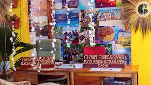 Un bureau avec des panneaux indiquant « Choum Tours », « Excursions et safaris » et « Service de navettes », entouré de chaises en osier et agrémenté d’une plante en pot.