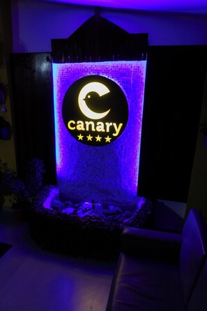 Un letrero con la palabra 'canary' y un logo con forma de creciente lunar, sobre una pared texturizada con diseño de ladrillo.