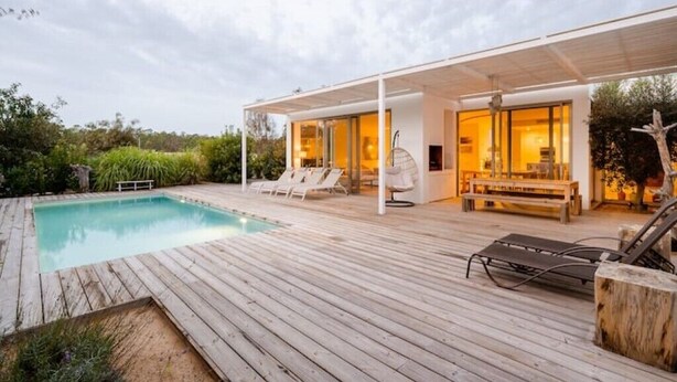 A modern outdoor pool area with a wooden deck, lounge chairs, and a covered seating area. - Eco-Luxe Villa Laranjeiras Comporta - Pool & Golf (comporta)