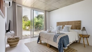 A modern bedroom with a large bed, a wooden headboard, a view of greenery outside, and a concrete ceiling. - Eco-Luxe Villa Laranjeiras Comporta - Pool & Golf (comporta)