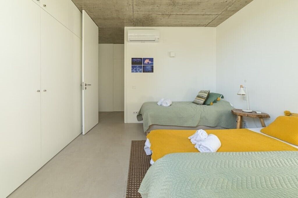 A bedroom with two beds, a small bedside table with a lamp, and an air conditioning unit on the wall.