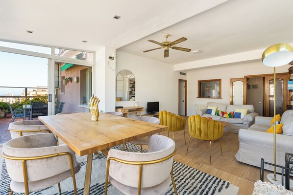 A spacious living area with a wooden dining table, comfortable seating, and a ceiling fan.