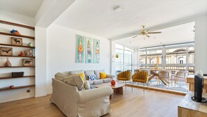 A spacious living room with a sofa, coffee table, and yellow chairs. There are shelves with decorative items and a large window with a view.