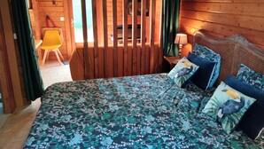 Ein Zimmer in einer Holzhütte mit Bett, Stuhl, Nachttisch und Fenster.