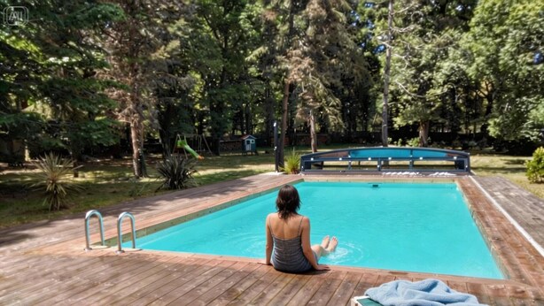 Ein Schwimmbecken mit Holzterrasse, Liegestuhl und einer kleinen Brücke darüber.