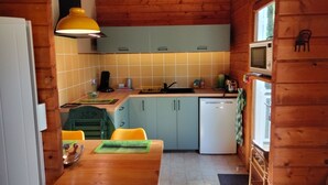 Eine kompakte Küche mit Holzwänden, einer gelben Hängelampe, einem Spülbecken, Schränken und einem kleinen Kühlschrank.