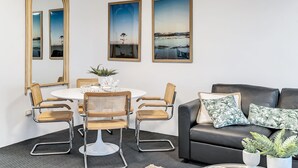 Uma sala de estar moderna com uma mesa de jantar redonda, quatro cadeiras de vime, um sofá de couro preto e três quadros de paisagens emolduradas.