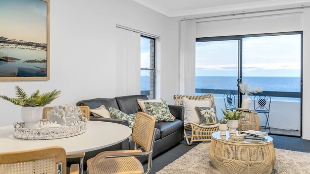 Uma sala de estar moderna com uma grande janela com vista para o mar, mobiliada com um sofá, cadeiras e uma mesa de jantar.