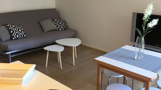Un salon moderne avec un canapé gris, deux petites tables rondes, une table à manger avec des chaises et un mur orné de noms de villes.