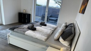A modern bedroom with a bed, bedside table, and a view of the outdoors. - Ferienhaus am Glück (Bad Zwischenahn)