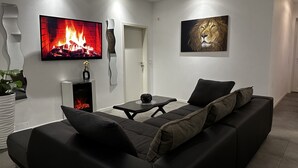 A modern living room with a black sofa, a flat-screen TV, a fireplace, and a lion painting. - Ferienhaus am Glück (Bad Zwischenahn)