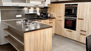 A modern kitchen with a central island, stainless steel appliances, and wooden cabinetry. - Ferienhaus am Glück (Bad Zwischenahn)