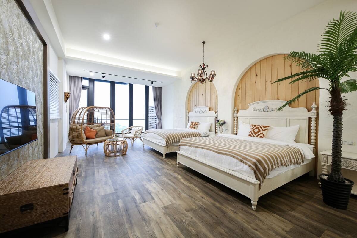 Un dormitorio con dos camas, televisor, un ventanal grande y una planta en maceta.
